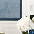 Blue coloured motorized blinds with a vase of flowers in the foreground.