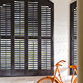 Urban storm window shutters in a painted brickwork room, with orange bicycle in the foreground.